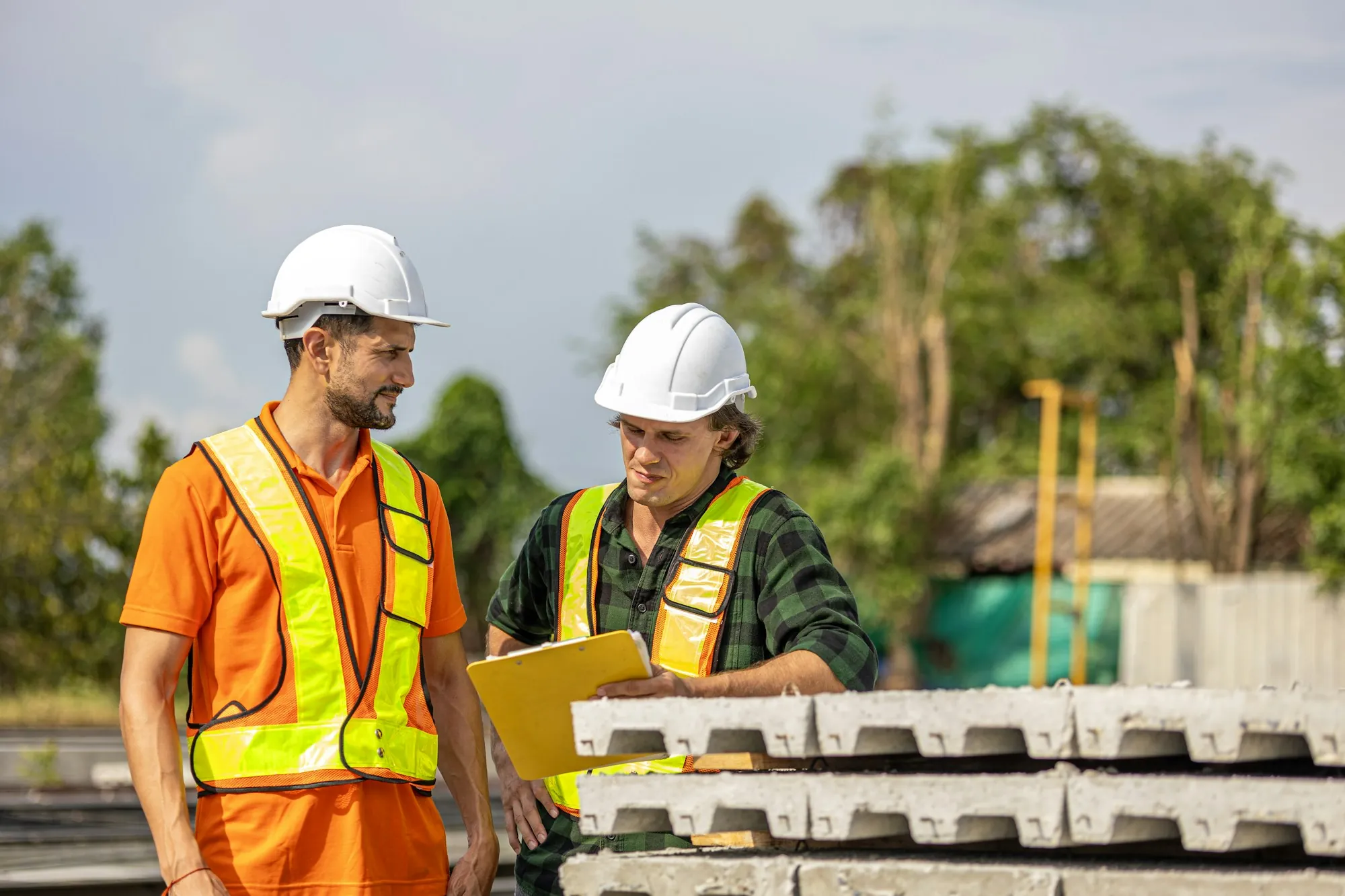 Two electricians in hard hats reviewing paperwork on site