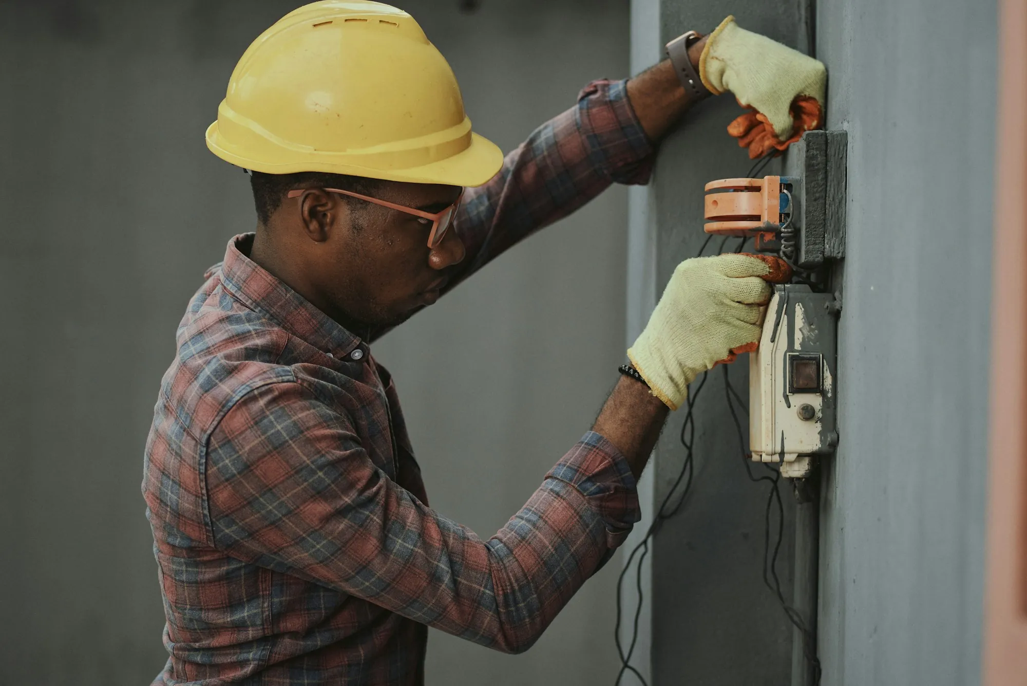 Electrician in a hard hat and gloves adjusting a meter on a residential panel