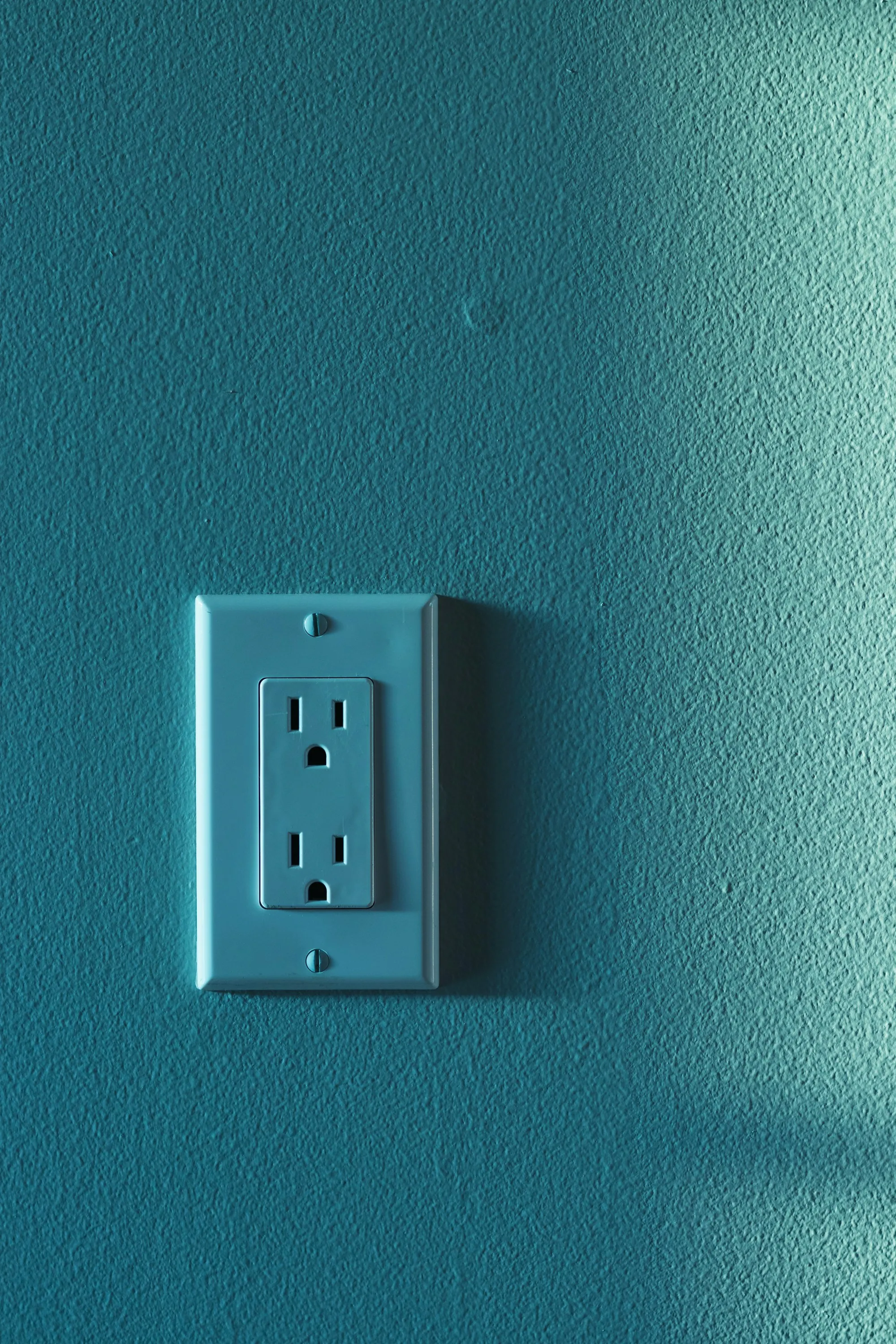 Teal painted wall with a single electrical outlet